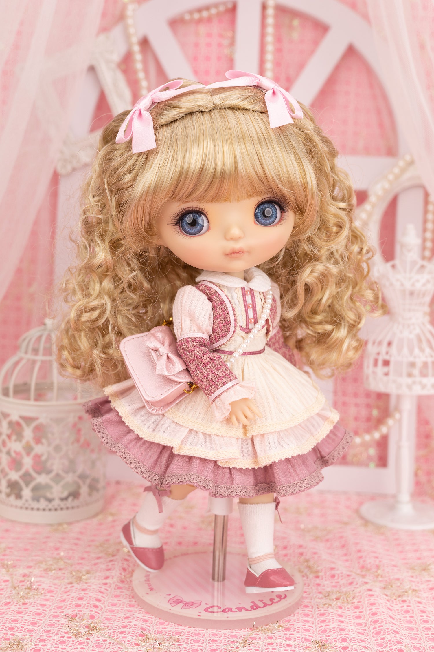 Candice doll with blonde hair and blue eyes wearing a pink and white outfit in a decorative setting.