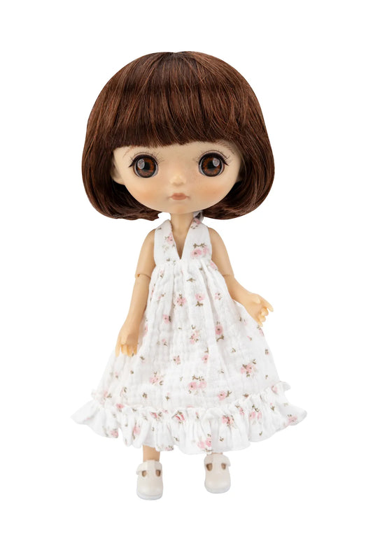 A doll with brown hair and large eyes wearing a white sleeveless dress with a pink floral pattern and white shoes, isolated on a white background.