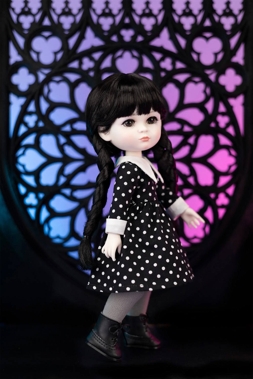 Doll in a black and white polka dot dress with long dark hair against a colorful geometric background