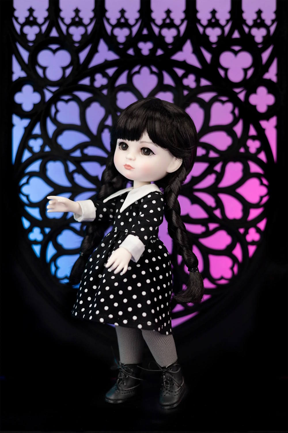 Doll in a black and white polka dot dress standing against a colorful geometric patterned background