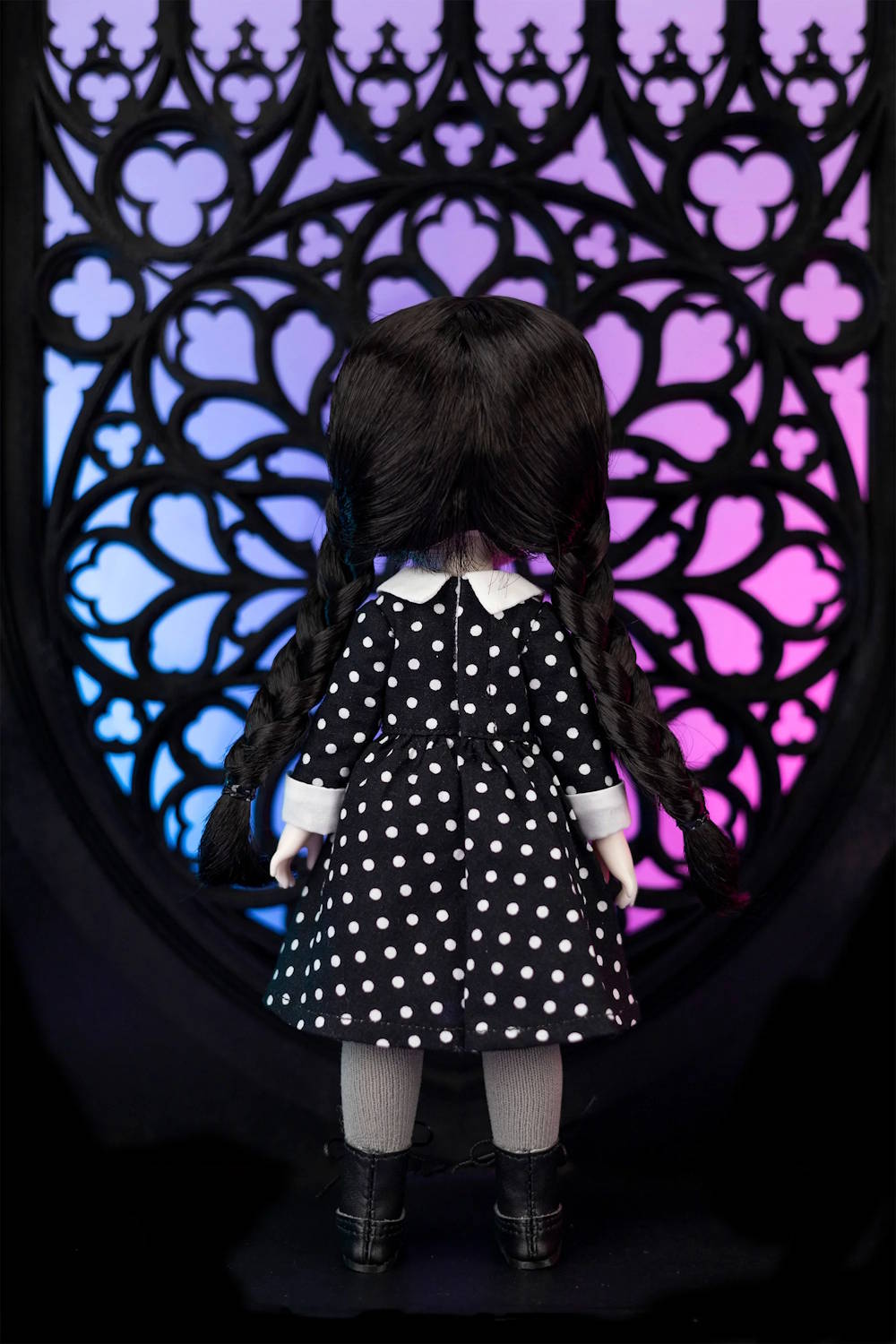Doll in a black and white polka dot dress standing in front of a decorative purple and pink background.