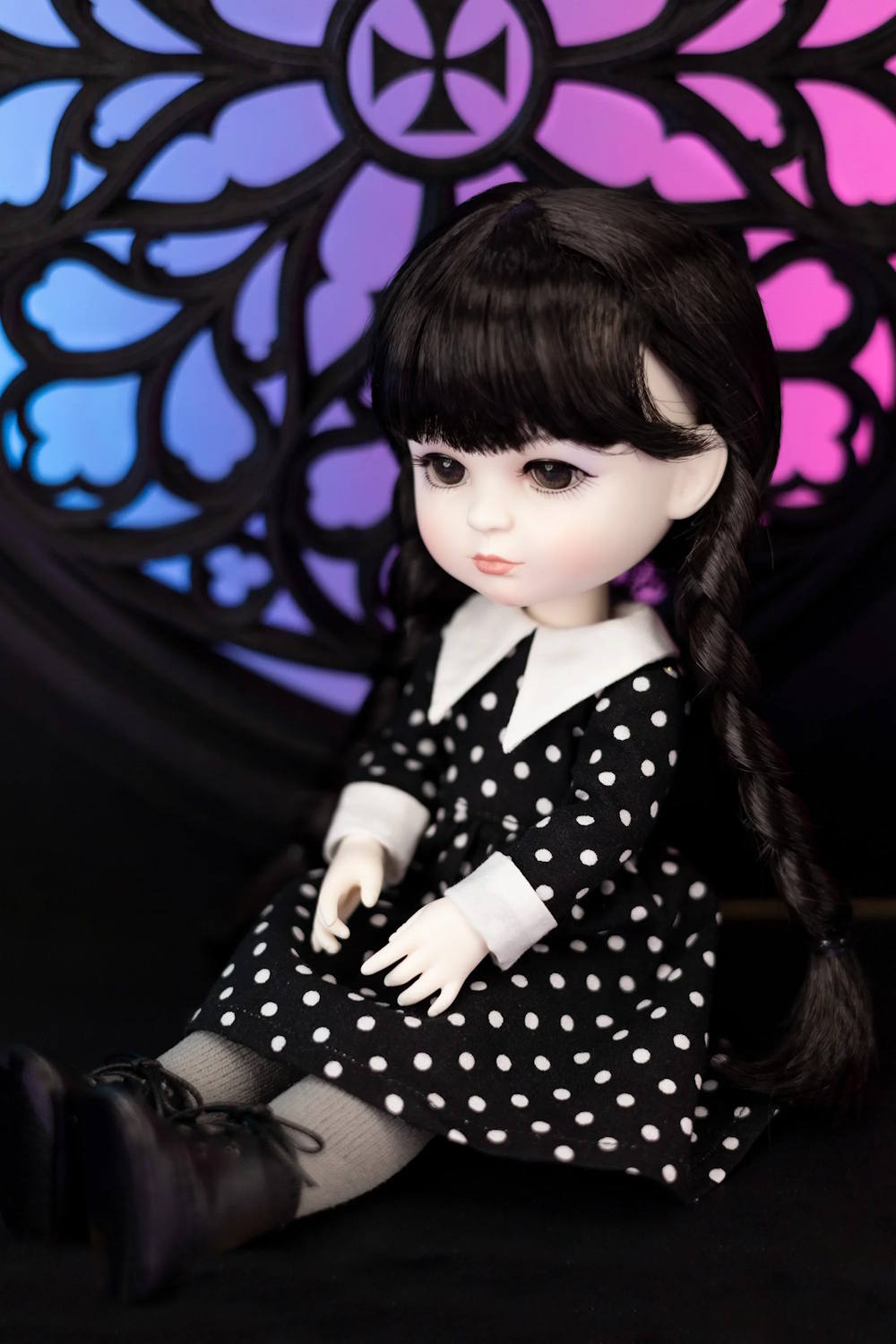 Doll in a black and white polka dot dress with a colorful stained glass window in the background