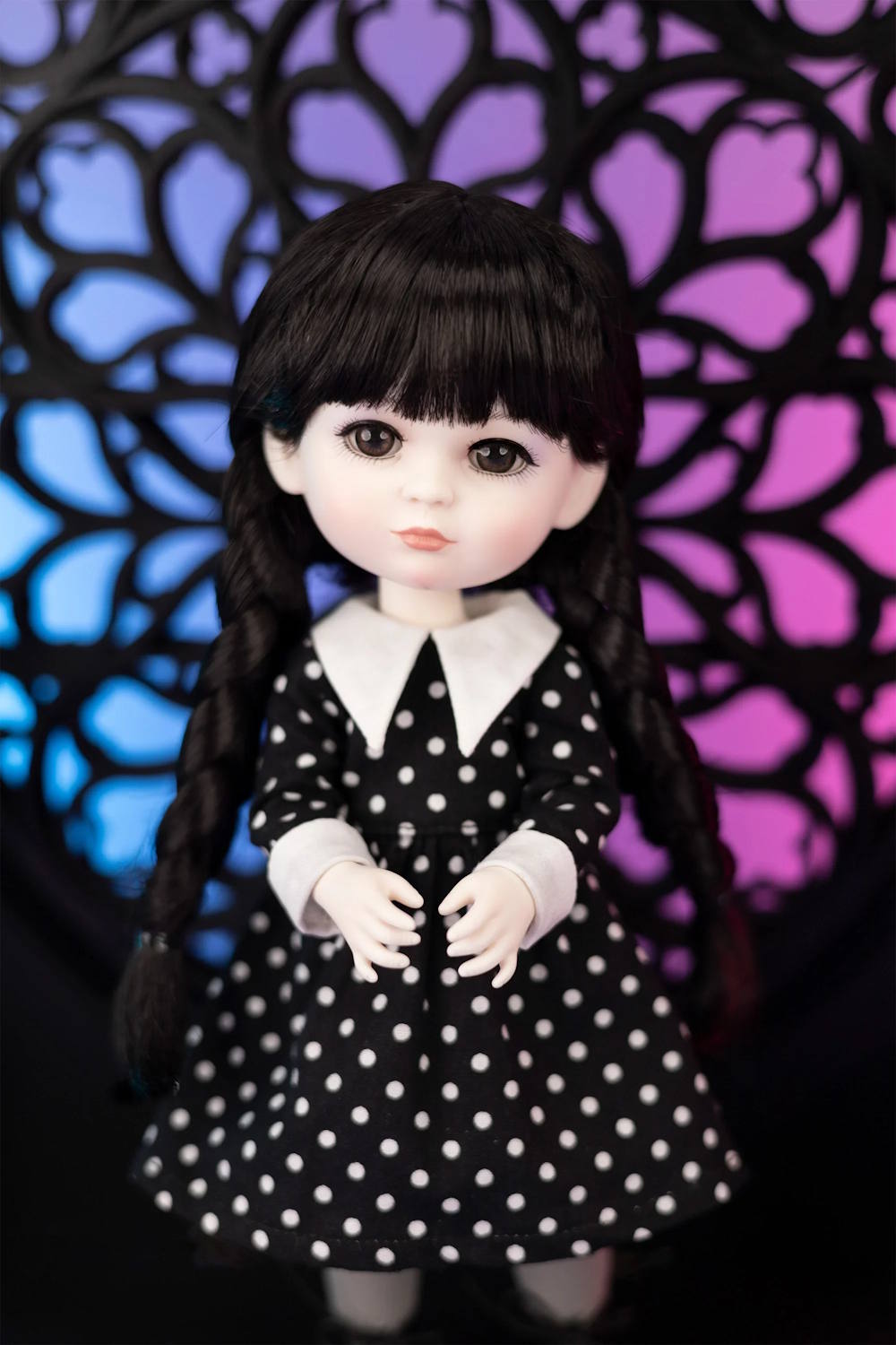 Doll in a black and white polka dot dress with braided hair against a colorful geometric background