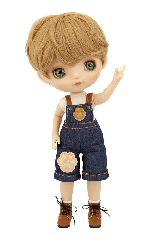 A stylized doll with short blond hair, large green eyes, and a raised right hand, wearing blue denim-style overalls with tan paw-print patches, a white shirt, brown socks, and brown lace-up boots on a plain white background.