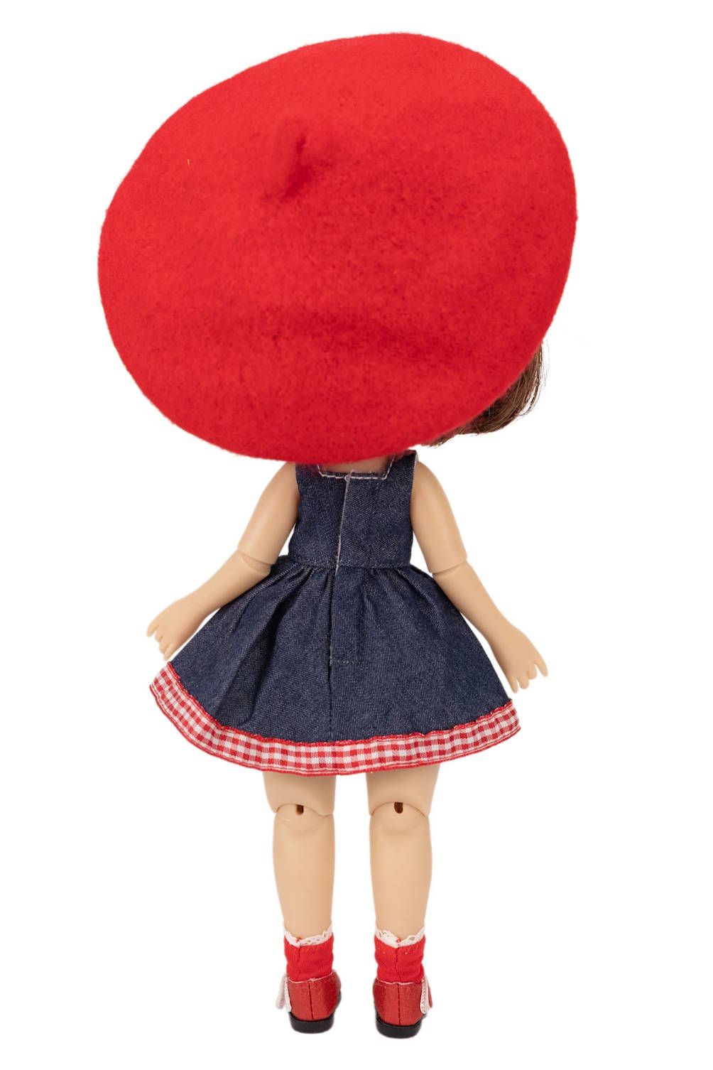 Doll wearing a red beret, denim dress with a checkered skirt, and red shoes on a white background