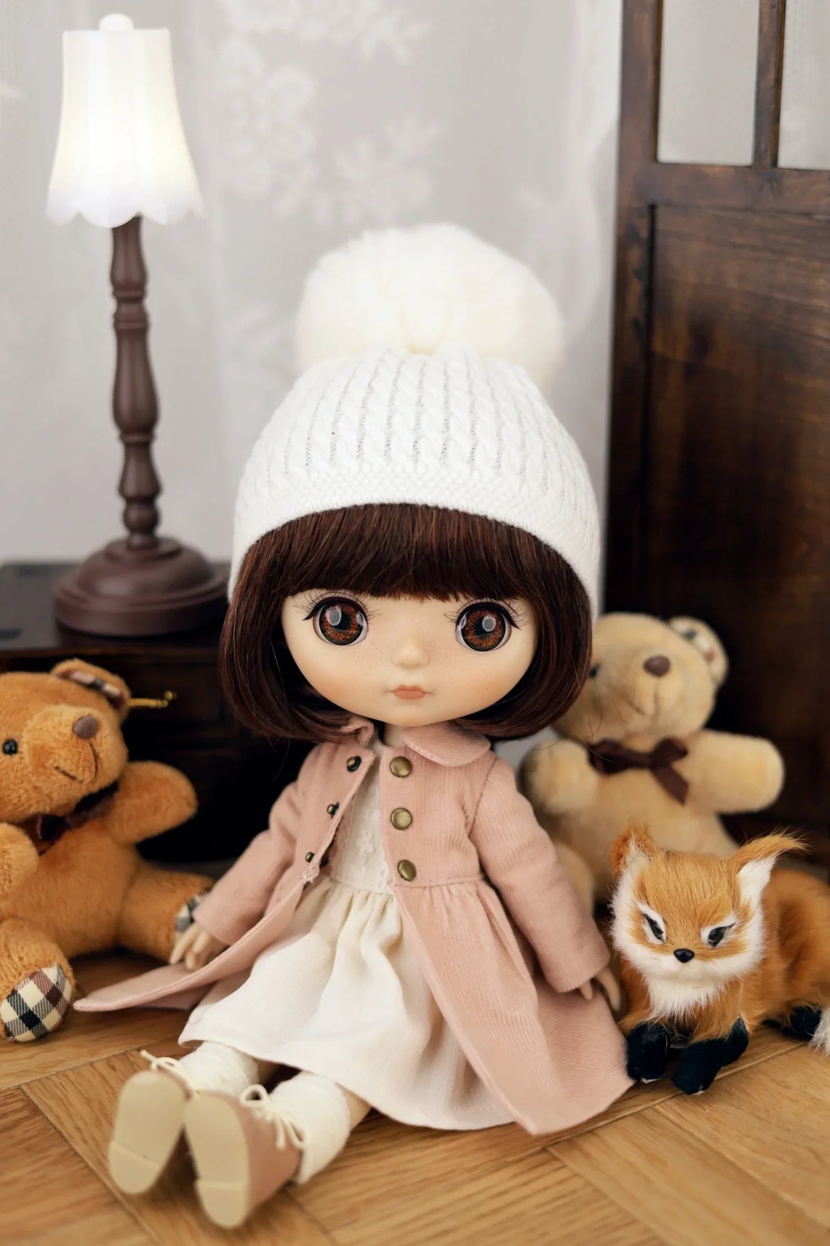 Doll wearing a white coat and hat with teddy bears and a fox in the background
