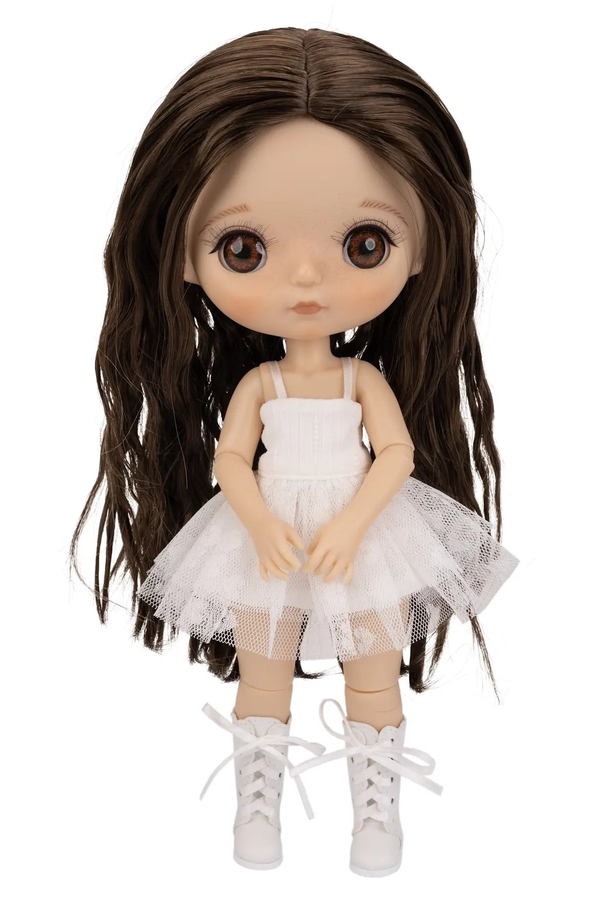 A doll with long dark brown wavy hair, large brown eyes, and a white sleeveless tutu dress with white lace-up shoes, shown against a plain white background.