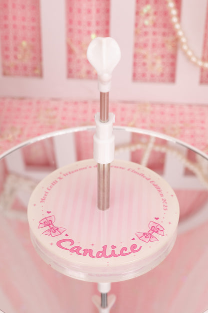 Round pink doll stand with 'Candice' written on a stand against a pink background