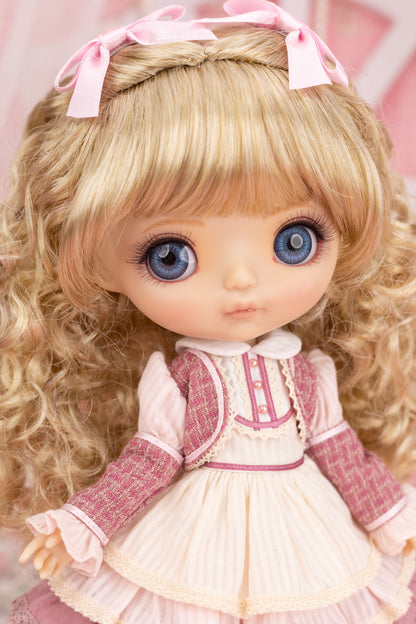 Candice doll with blonde hair and blue eyes wearing a pink and white dress against a blurred background