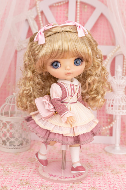 Candice doll with blonde hair and blue eyes wearing a pink and white outfit in a decorative setting.