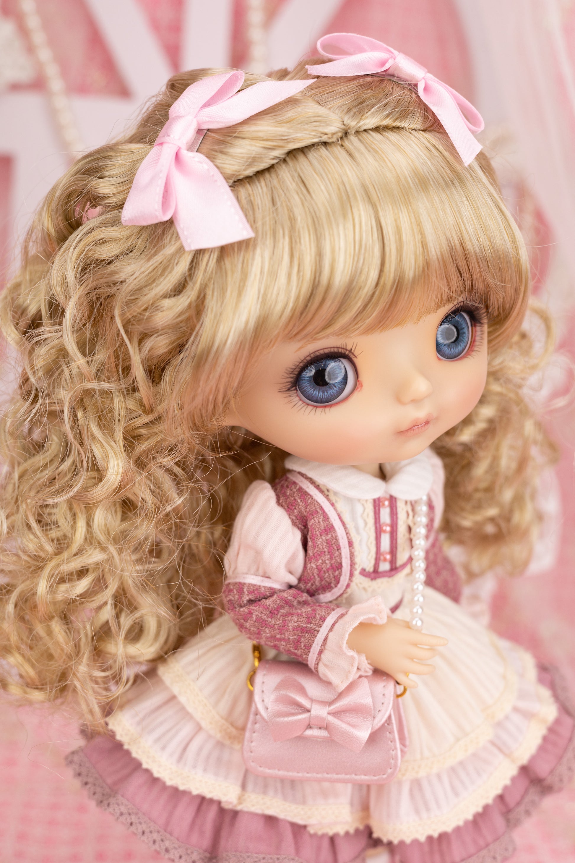 Candice doll with blonde hair and blue eyes wearing a pink and white outfit on a pink background