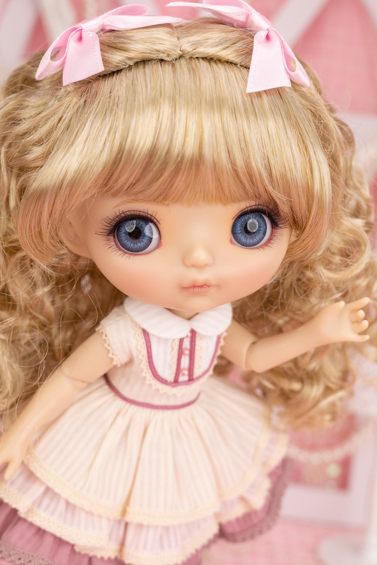 Candice doll with blonde hair and blue eyes wearing a pink dress with a bow on a blurred background
