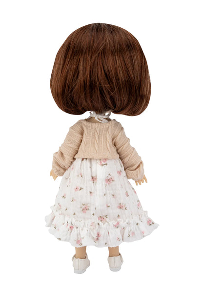 Back view of a doll with short brown hair, wearing a beige knit cardigan over a white ruffled skirt with a pink floral print, and white shoes, on a white background.