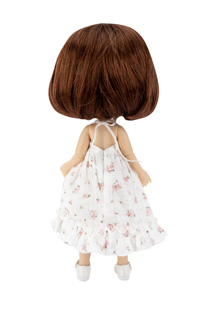 A doll viewed from the back, featuring short brown hair and wearing a white sleeveless ruffled dress with a pink floral pattern and white shoes, isolated on a white background.