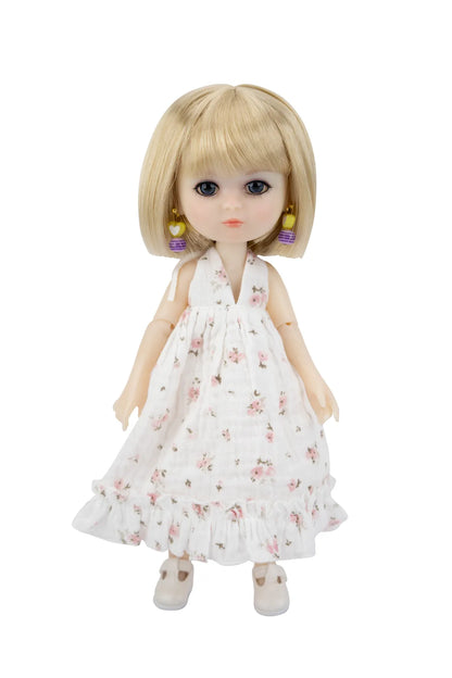 A blonde doll with large blue eyes wearing a white sleeveless dress with a pink floral print, standing against a plain white background.