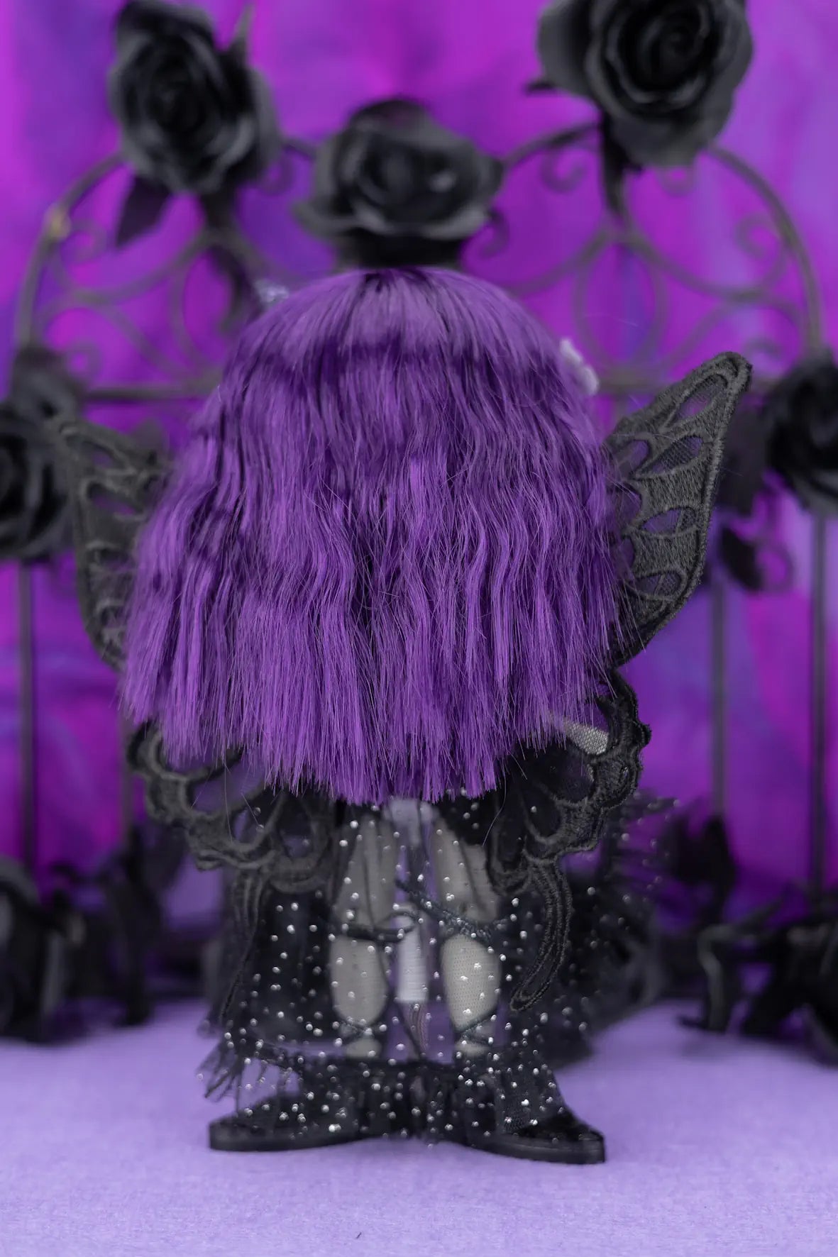 Doll with purple hair and black wings against a purple background