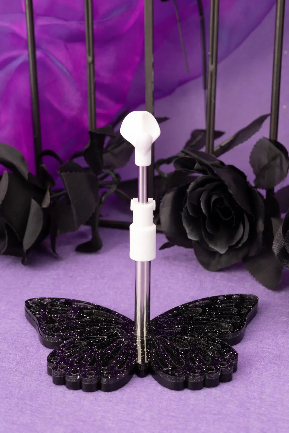 Butterfly-shaped doll stand on a purple surface with black roses in the background