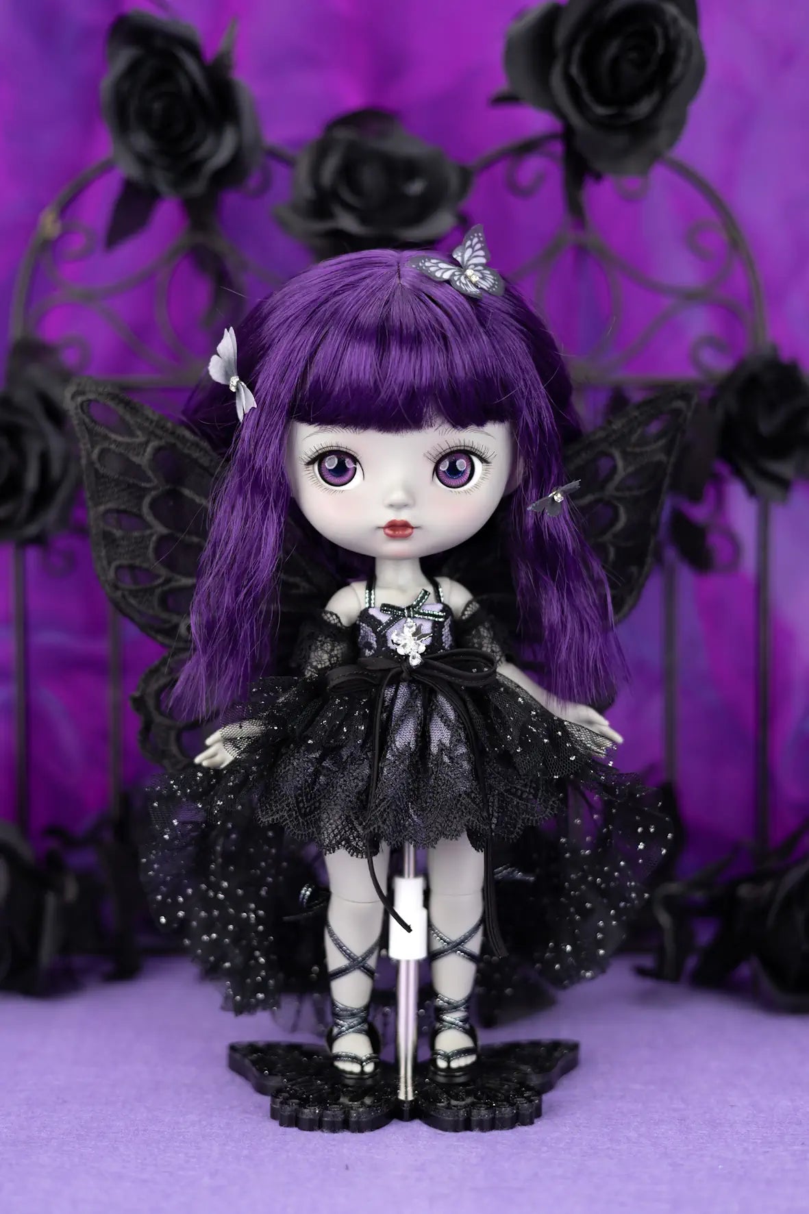 Gothic-style doll with purple hair and black outfit against a purple background with black roses.