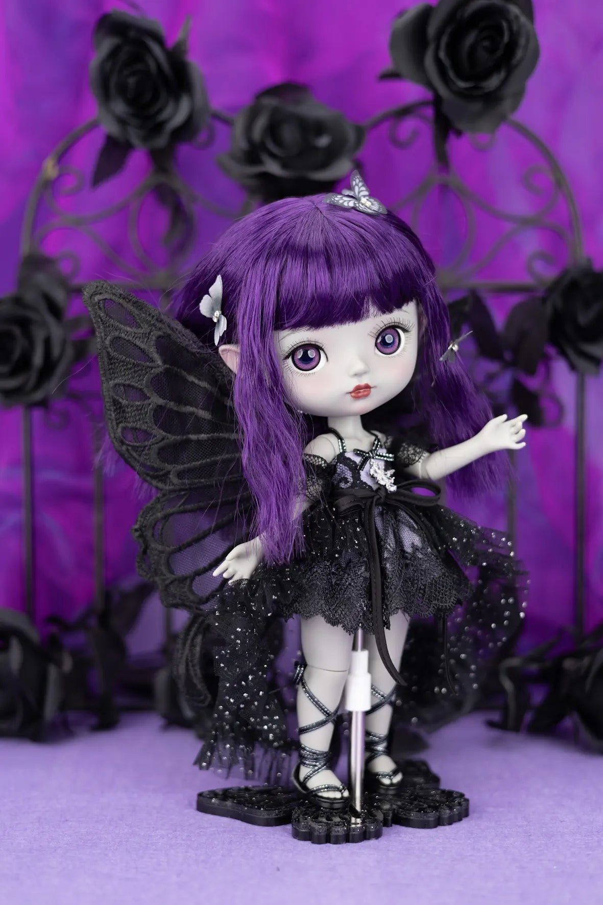 Gothic-style doll with purple hair and black wings against a purple background with black roses.
