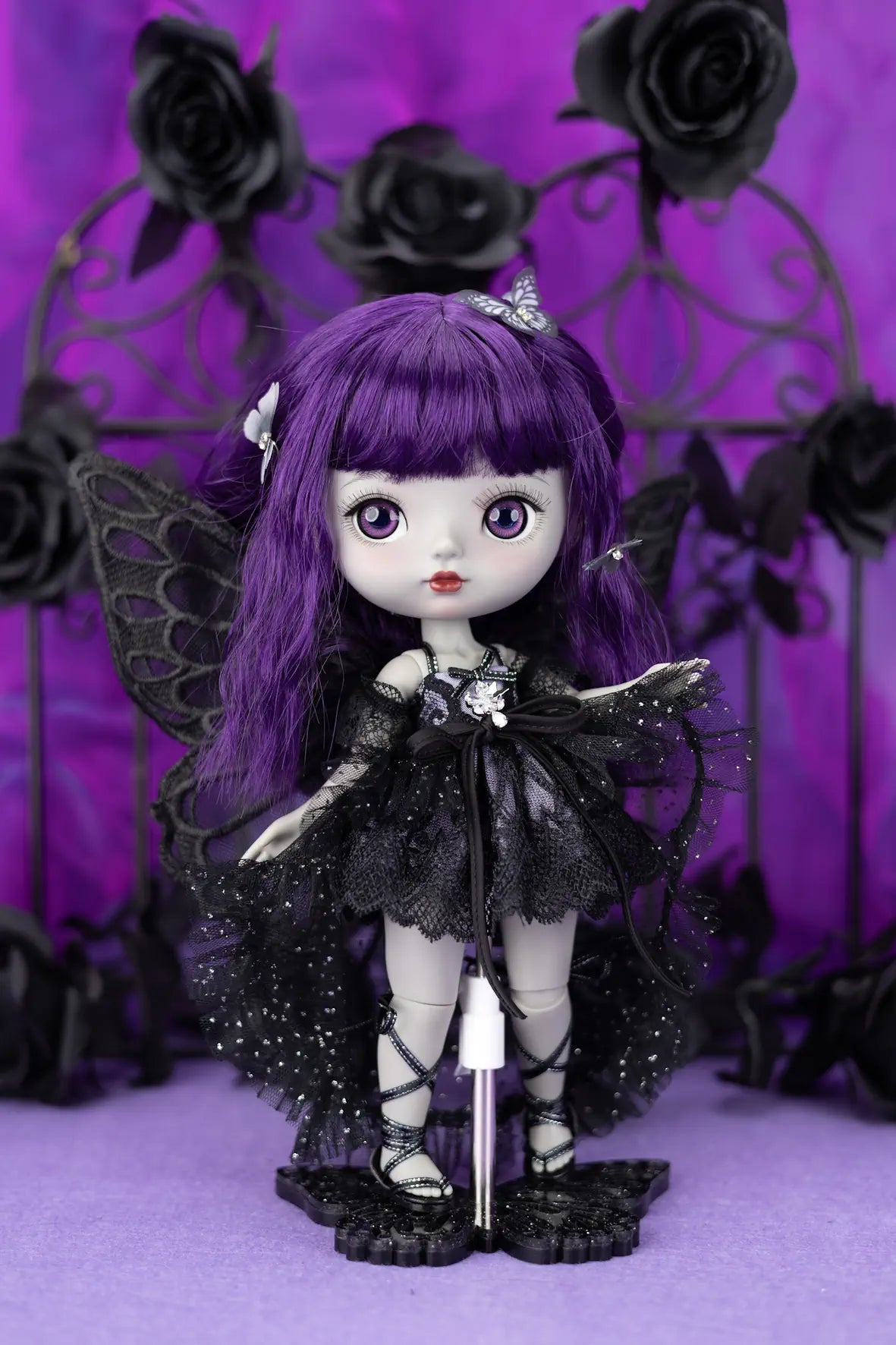 Gothic-style doll with purple hair and black outfit against a purple background with black roses.