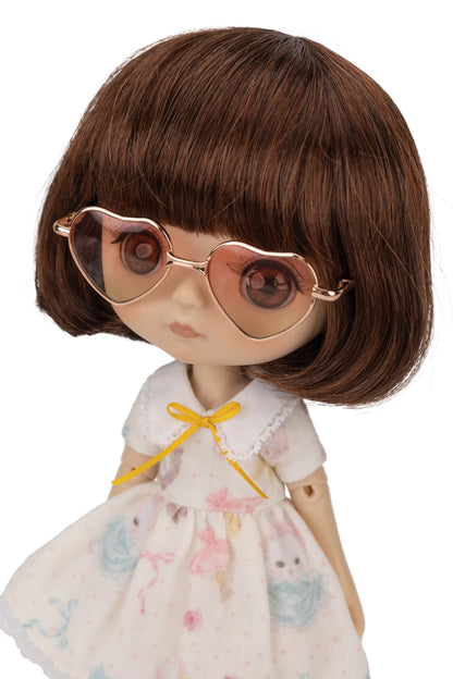 Doll with brown hair, heart-shaped amber sunglasses, and a white dress with colorful patterns on a white background