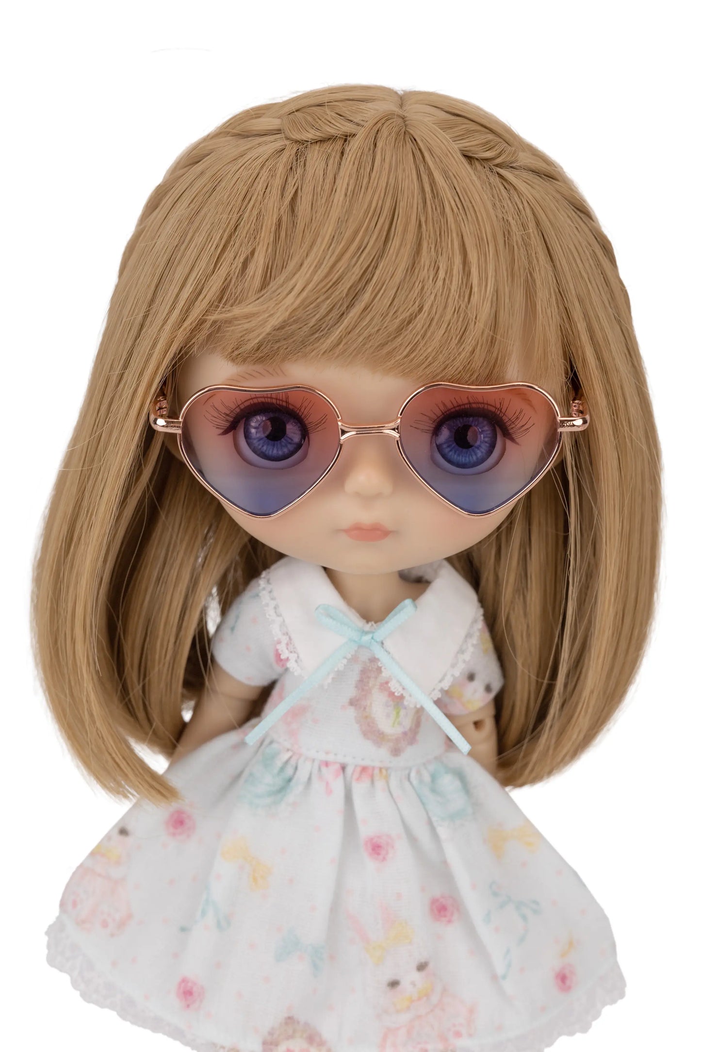 Doll with blonde hair and a floral dress wearing heart-shaped blue gradient sunglasses on a white background