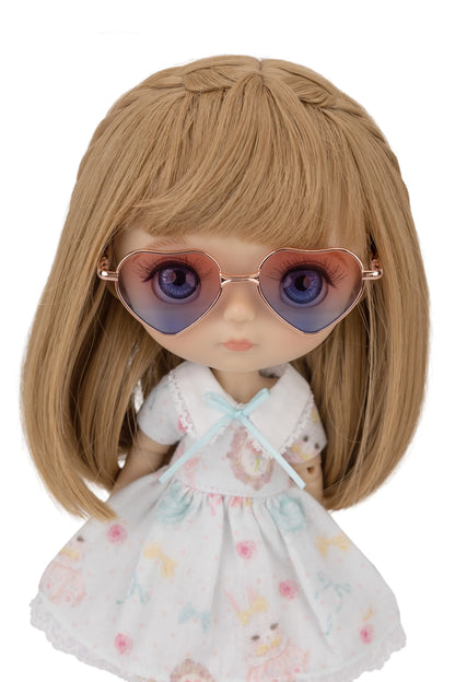 Doll with blonde hair and a floral dress wearing heart-shaped blue gradient sunglasses on a white background