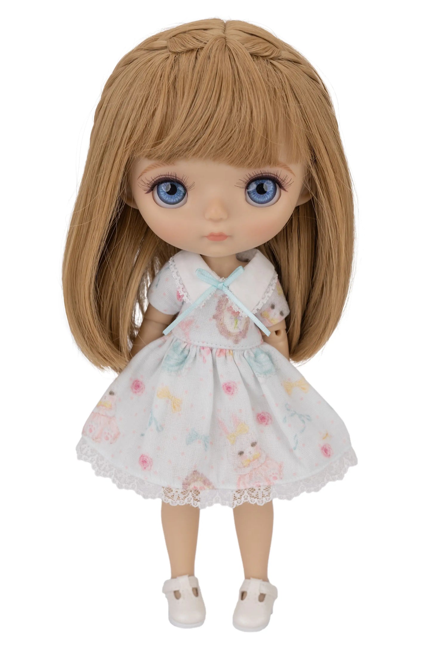Doll with long brown hair wearing a white dress with floral and bunny patterns on a white background
