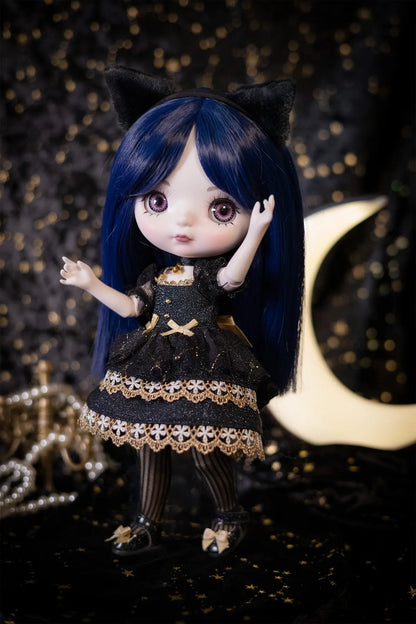 A doll with long dark blue hair, black cat ears, and a black dress with gold lace trim stands against a dark background with gold bokeh lights and a crescent moon prop.