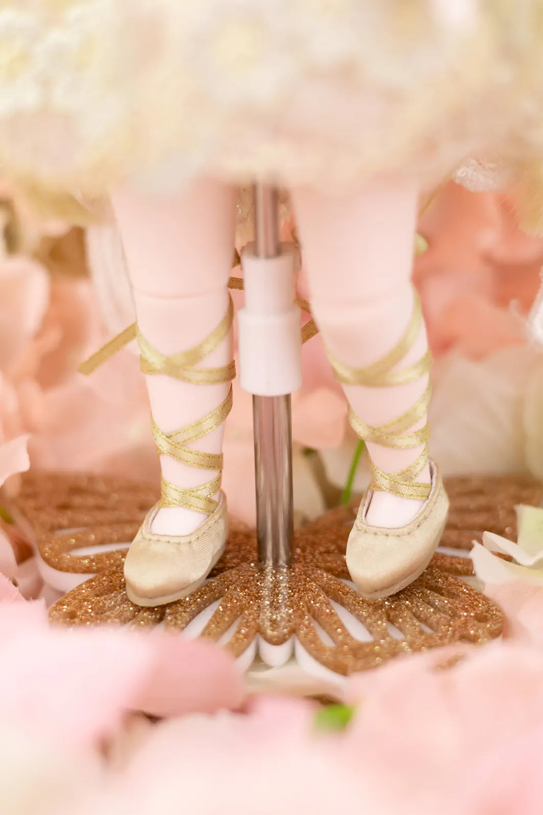 Close-up of a doll's feet in gold shoes and tights on a glittery surface with blurred background
