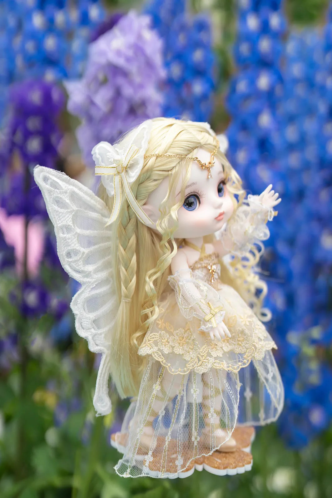 Fairy figurine with wings and a dress in front of blue flowers