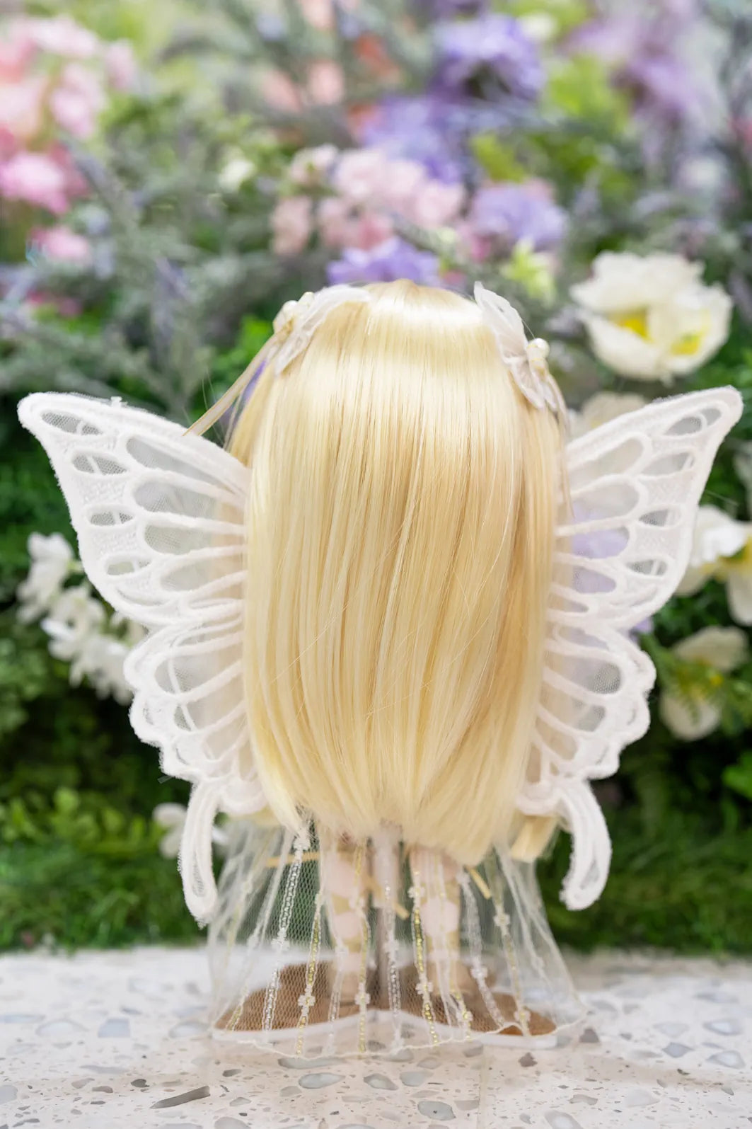 Doll with blonde wig with butterfly wings on a floral background