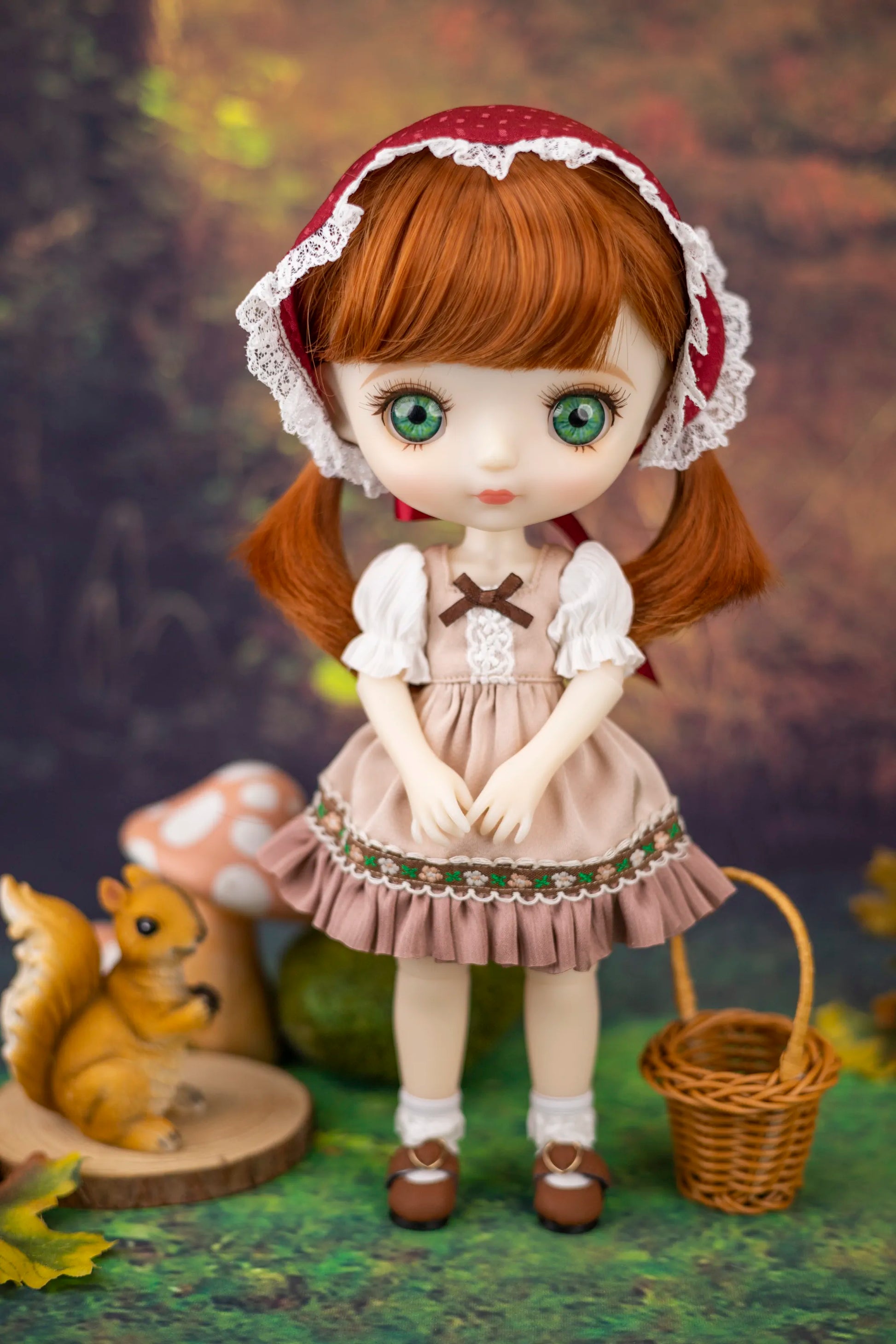 Doll with ginger hair and a brown dress standing in a forest setting with a squirrel and basket.