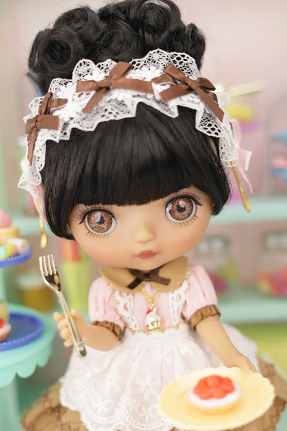 Doll with black hair, lace headband, and pink dress holding a fork and plate with food.