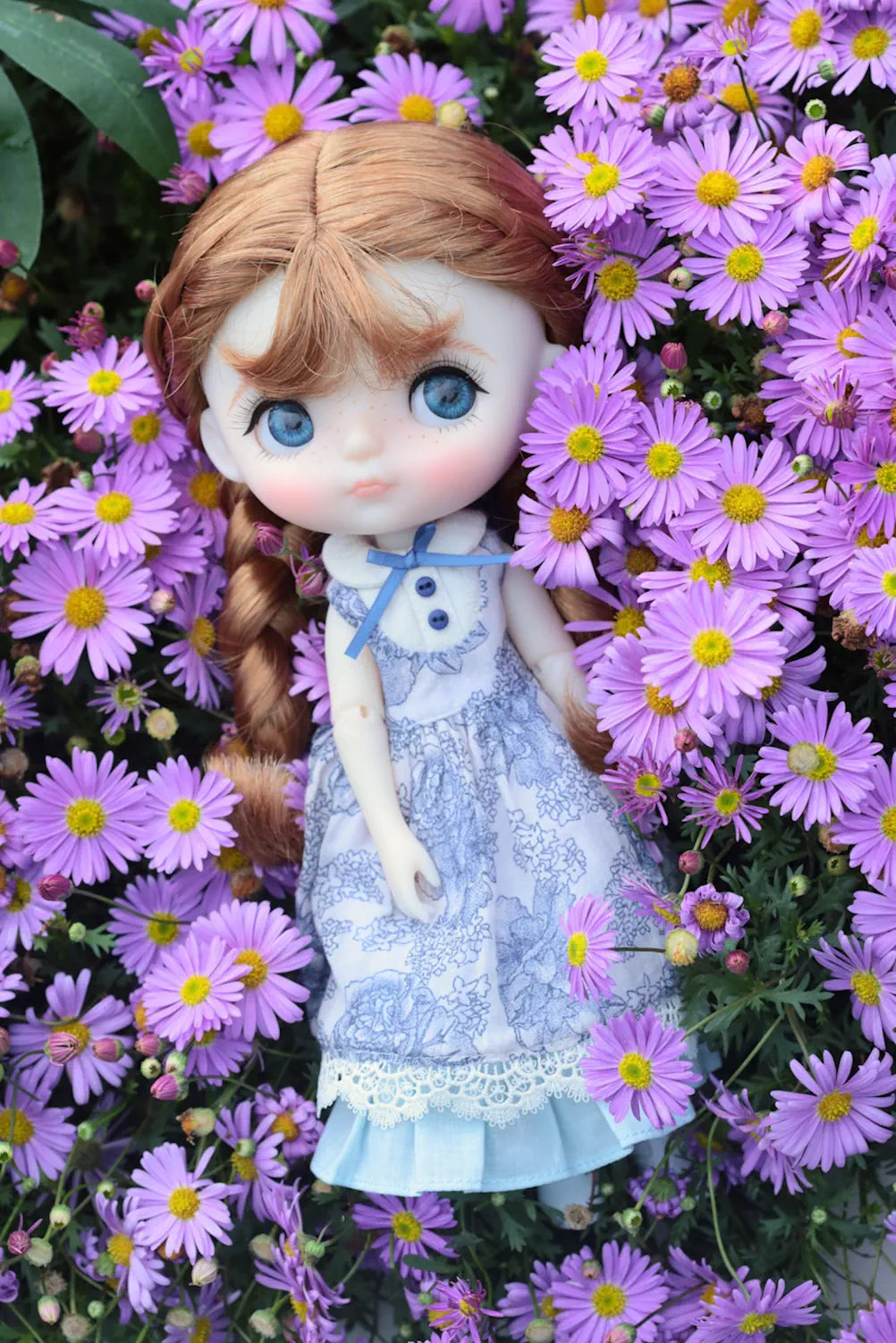Doll with braided hair and blue dress surrounded by purple flowers