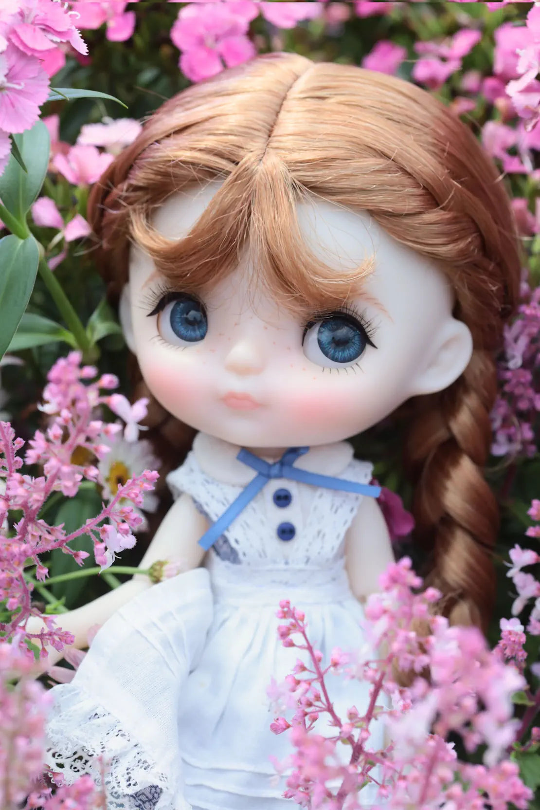 Doll with braided hair and blue eyes surrounded by pink flowers