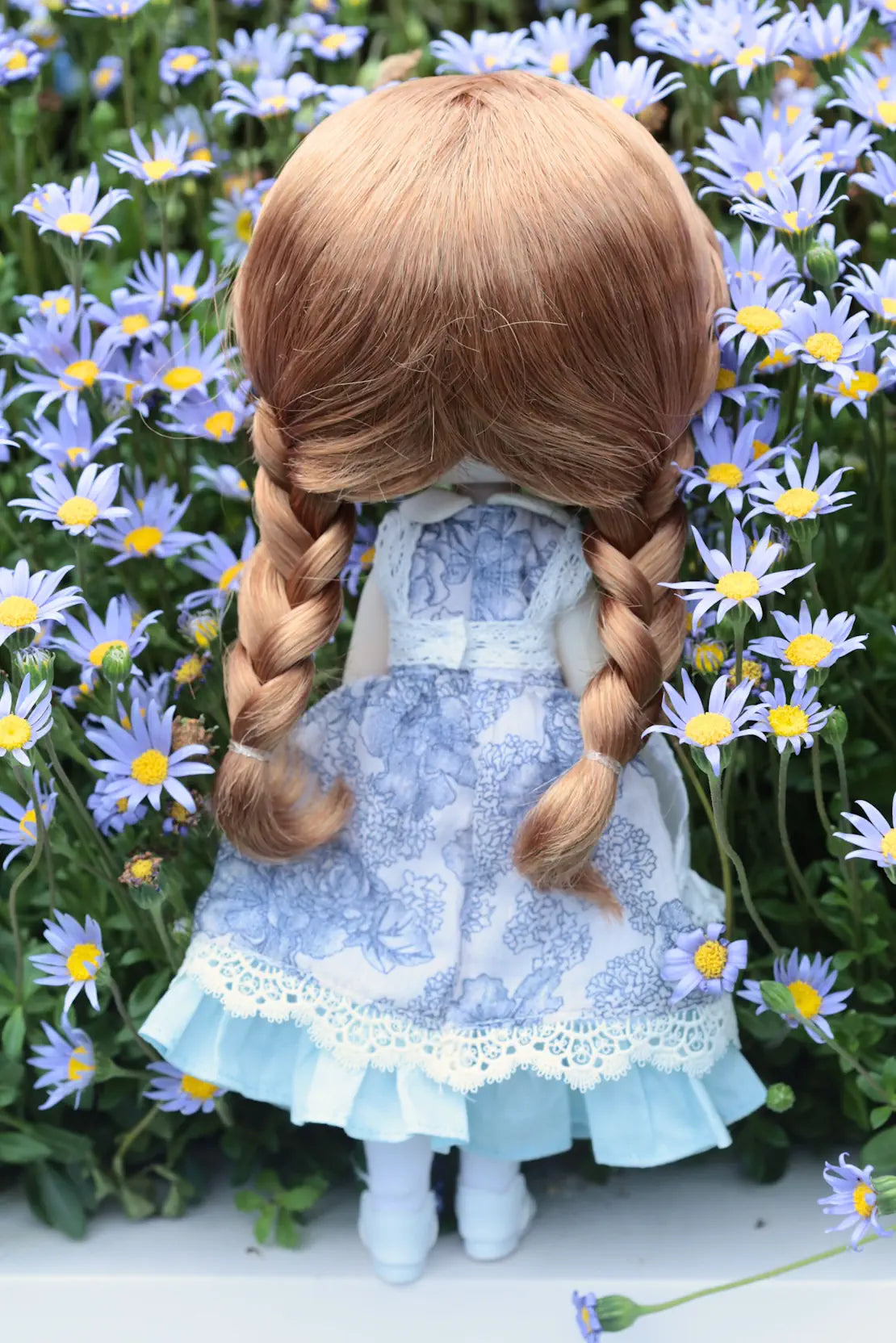 Doll with braided hair and a blue dress standing among flowers