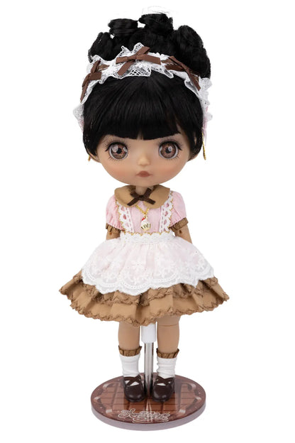 A doll with large brown eyes and black hair styled in a messy bun with a lace headband, wearing a pink and brown ruffled dress with white lace trim, standing on a round display base against a white background.
