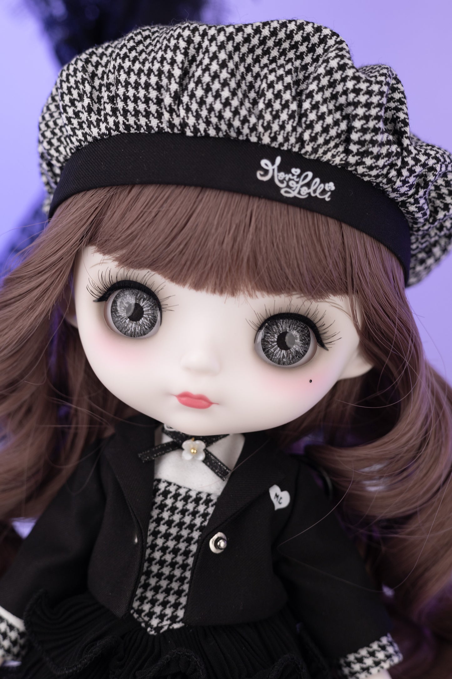 Doll with houndstooth pattern hat and coat against a purple background