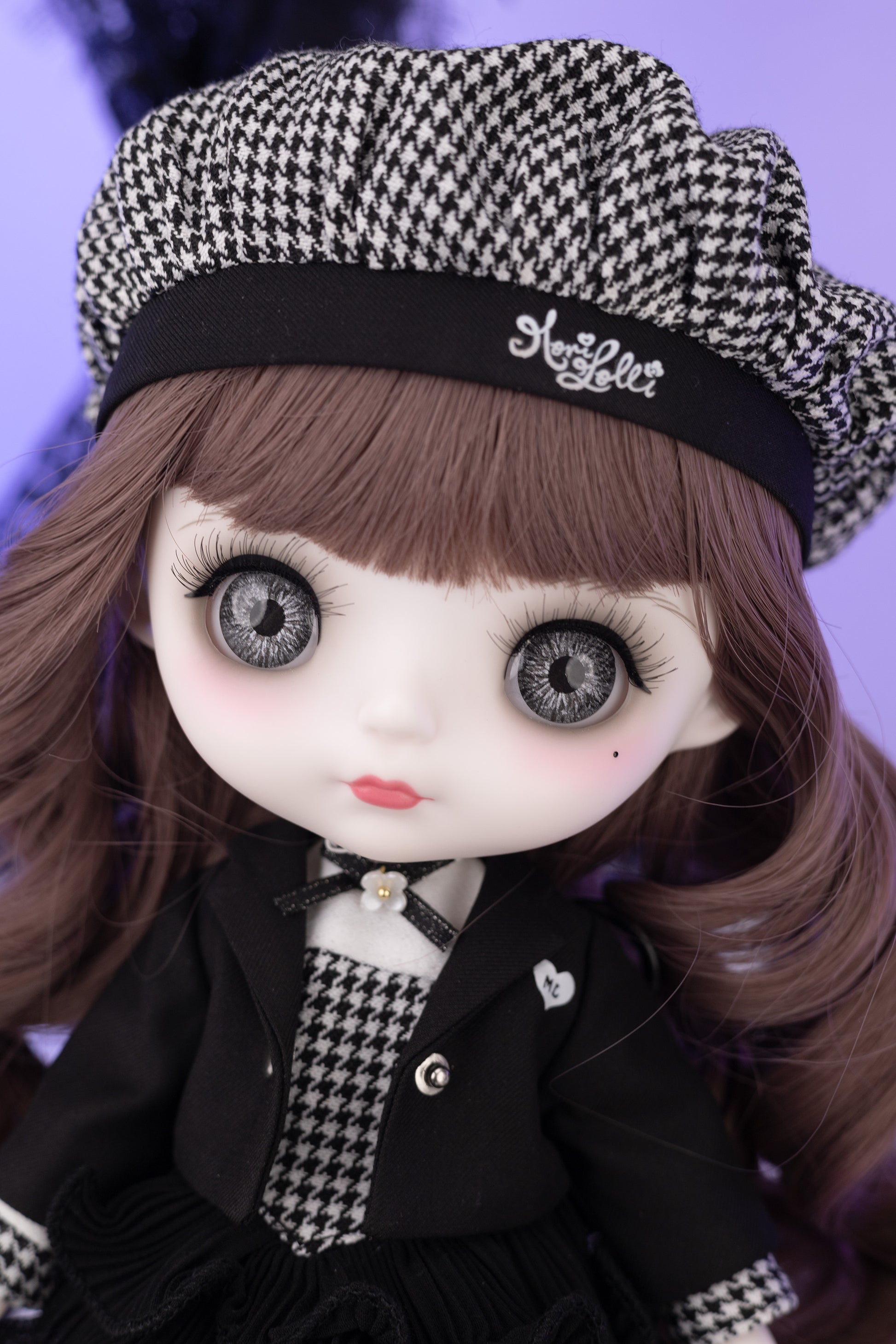 Doll with houndstooth pattern hat and coat against a purple background