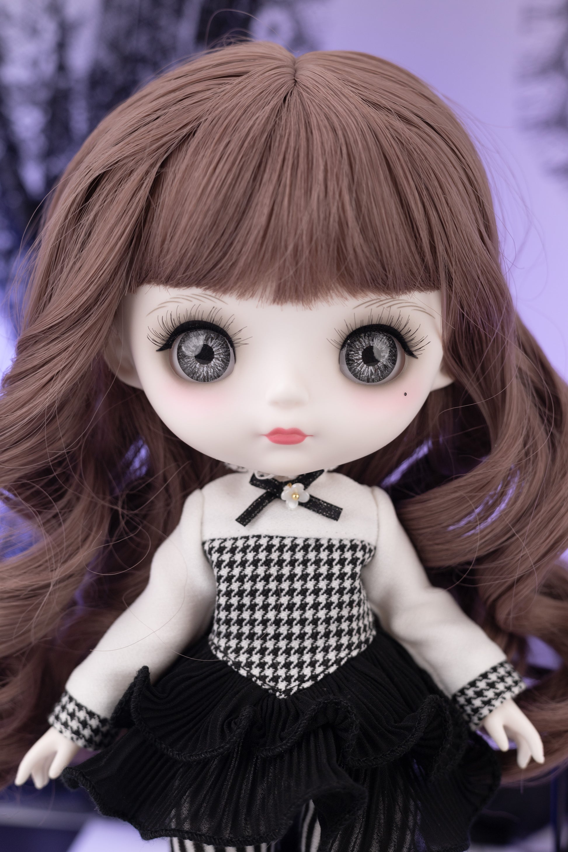 Doll with long brown hair and large eyes wearing a black and white checkered outfit.