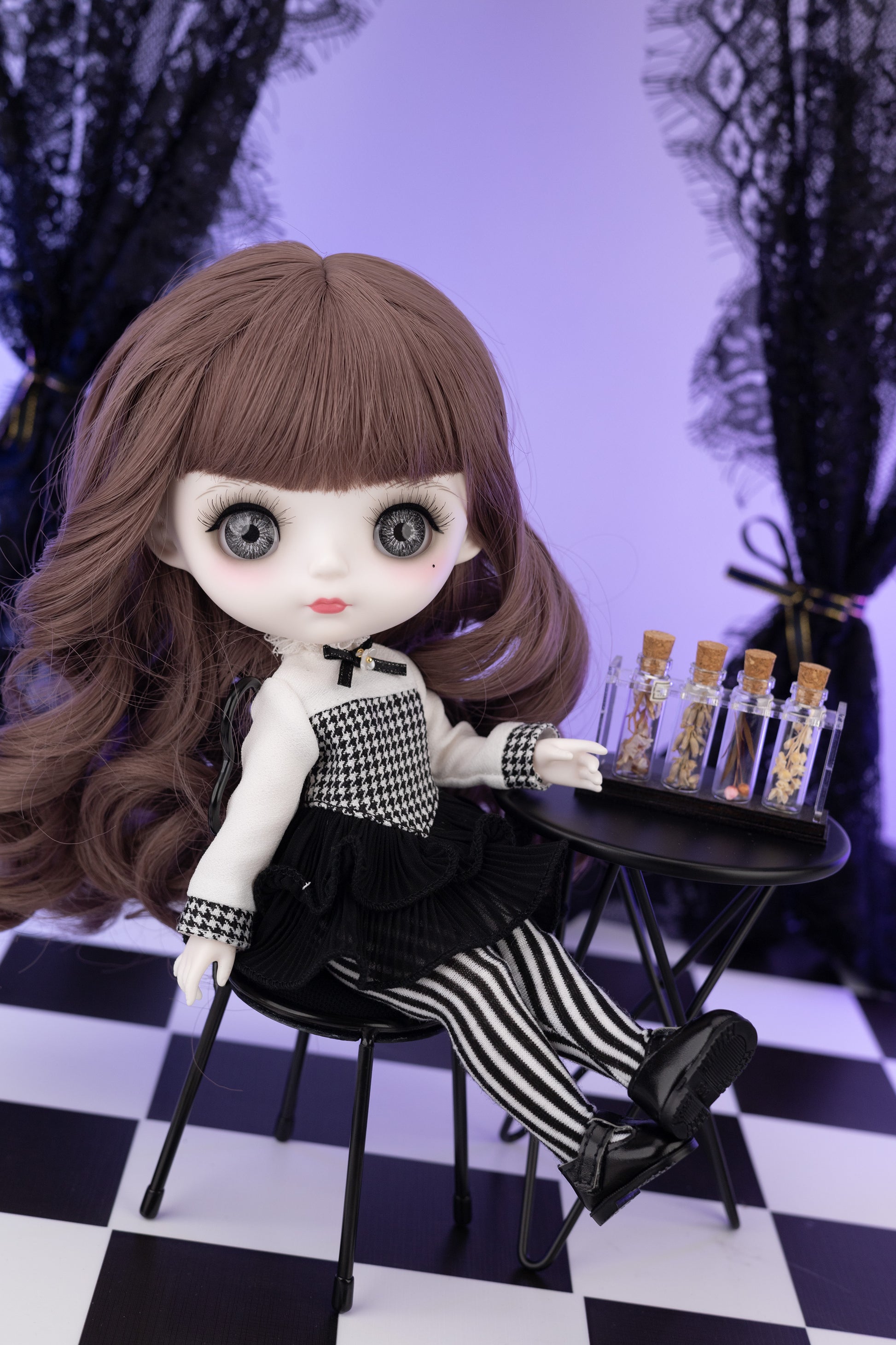 Doll with long brown hair and checkered outfit sitting on a chair with a small table in a checkered room.