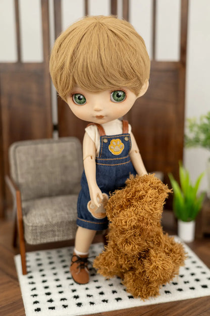 A doll with blonde hair and green eyes, wearing denim overalls and a white shirt, holding a brown plush dog toy in a miniature room setting.