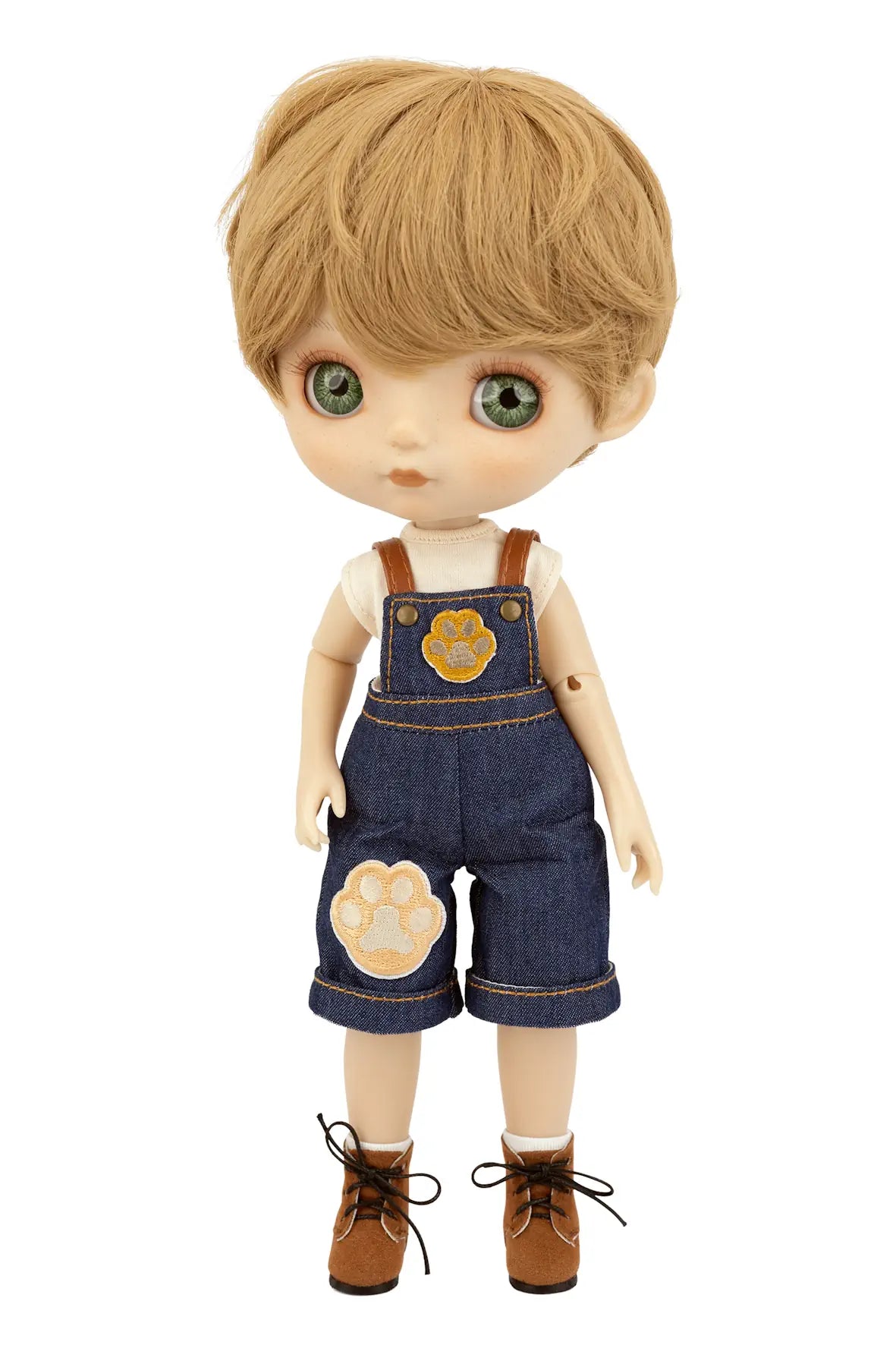 A doll with blonde hair and green eyes, wearing blue denim overalls with tan paw-print patches, a white shirt, and brown shoes, shown against a plain white background.