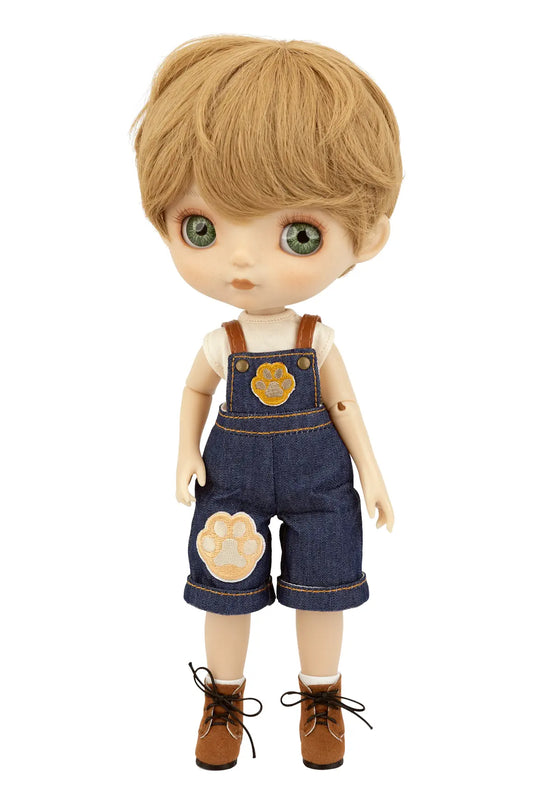A doll with blonde hair and green eyes, wearing blue denim overalls with tan paw-print patches, a white shirt, and brown shoes, shown against a plain white background.
