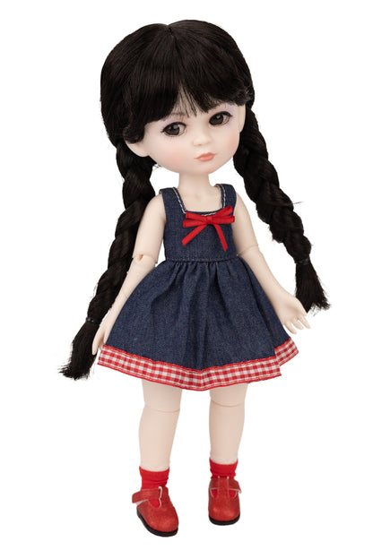 Doll with black hair in pigtails wearing a denim dress with a red bow and red shoes on a white background