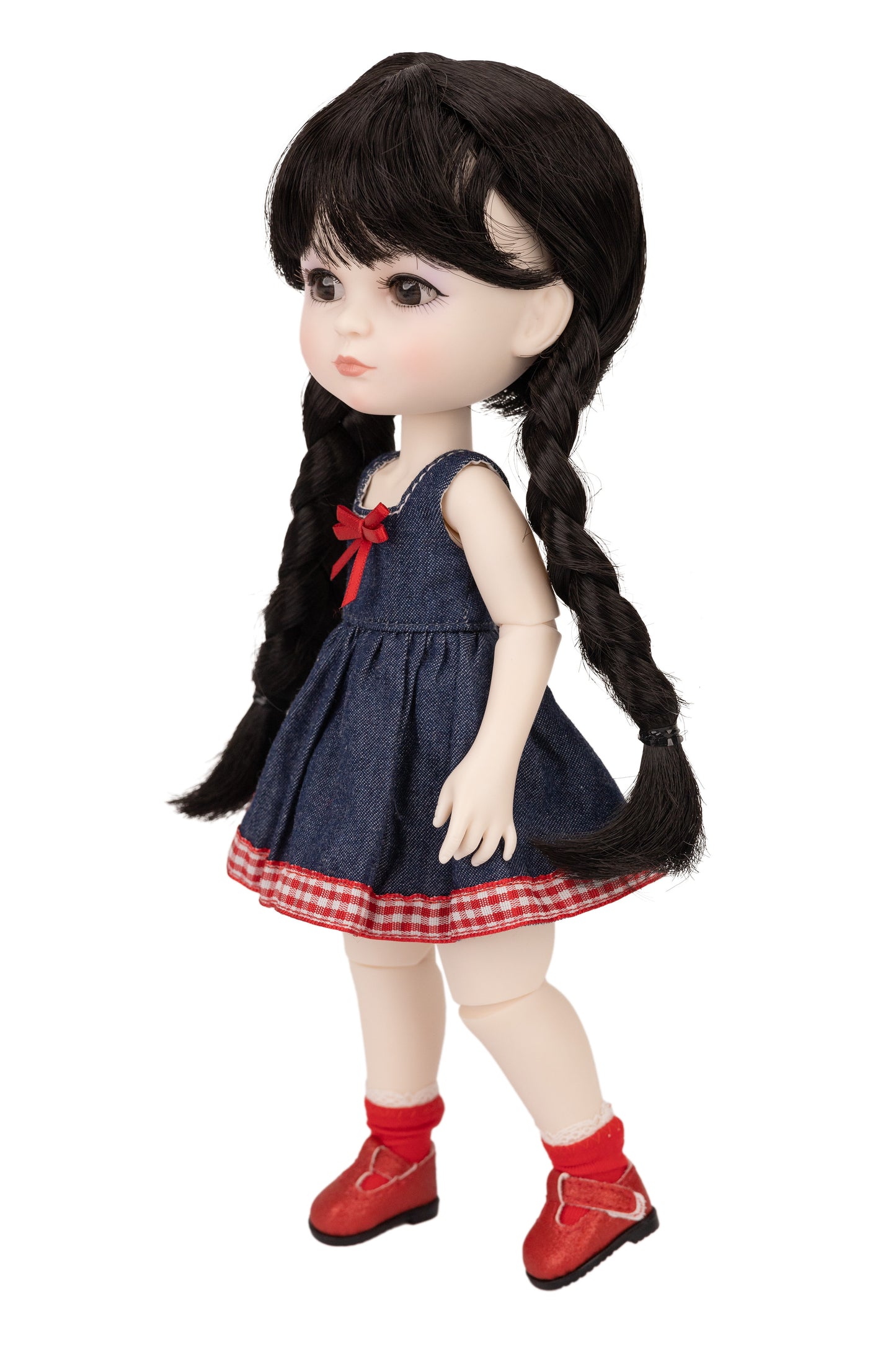 Doll with long braided hair wearing a denim dress with a red plaid skirt and red shoes on a white background