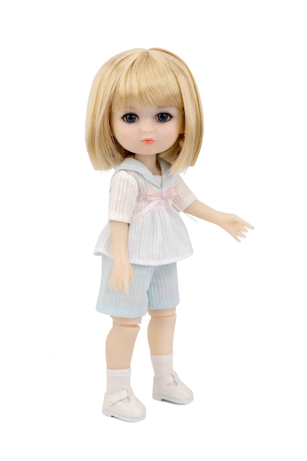 A Luna Lily doll with large dark eyes wearing a white and light blue outfit with a pink bow, standing against a plain white background.