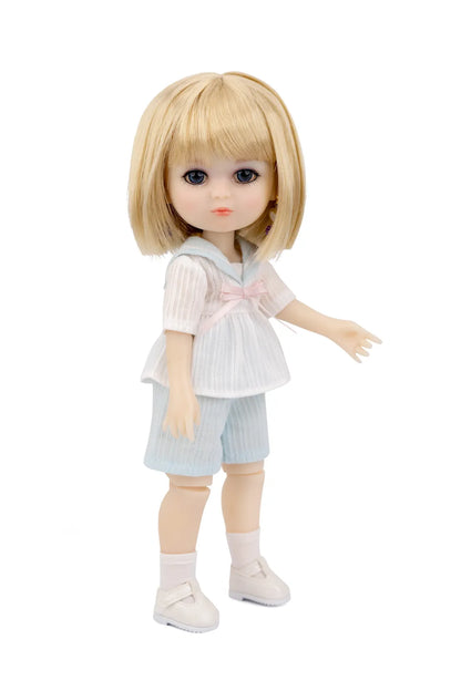 A Luna Lily doll with large dark eyes wearing a white and light blue outfit with a pink bow, standing against a plain white background.