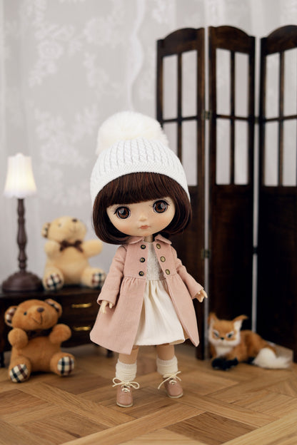 Doll wearing a pink coat and white hat in a room with toys and a lamp.